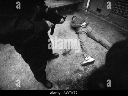 Uomo in piedi e puntamento sub-machine gun all uomo a faccia in giù sul pavimento, b&W Foto Stock