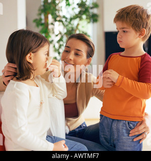 Donna con le braccia intorno a due bambini, guardando alla ragazza soffia il naso Foto Stock