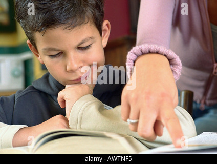 Bambino guardando a libro, donna di puntamento a mano in carta, vicino. Foto Stock