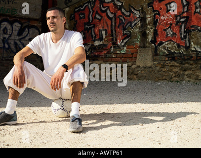 Uomo seduto sul pallone da calcio Foto Stock