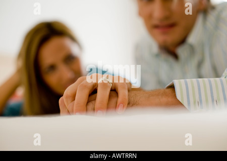 La mano di una donna con un anello di nozze tenendo un man mano che indossa una camicia bianca con blu e strisce gialle Foto Stock