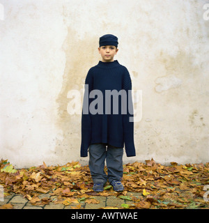 Ragazzo che sta tra foglie di autunno, indossa un maglione sovradimensionato Foto Stock