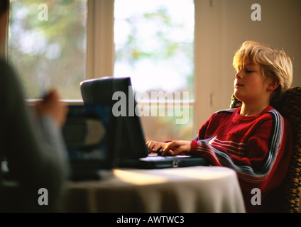 Ragazzo seduto a tavola utilizzando il computer, seconda persona sfocato in primo piano Foto Stock