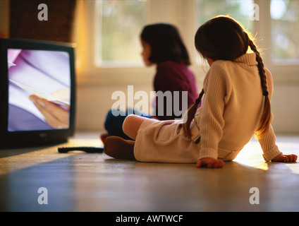 Le giovani ragazze seduta sul pavimento di legno guardando la TV, ragazza sullo sfondo sfocato Foto Stock
