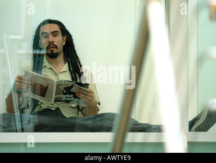 Uomo seduto a terra tenendo la rivista, cercando Foto Stock