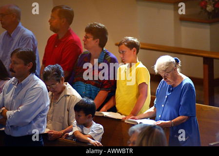 White pre teen boy prega con i genitori e la nonna durante la Messa cattolica Foto Stock