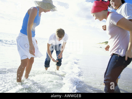 Quattro amici in piedi di surf, un uomo raccogliendo manciata di sabbia Foto Stock