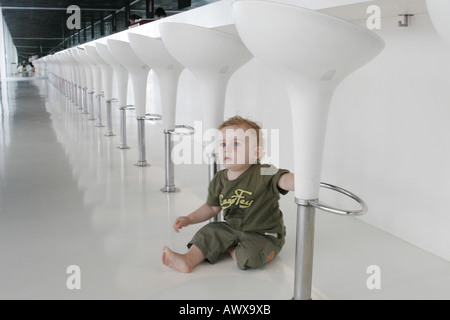 Piccolo Ragazzo seduto tra gli sgabelli da bar Foto Stock