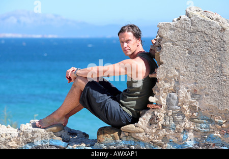 Bel uomo di mezza età seduto su un vecchio muro di pietra di sole Foto Stock