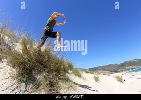 Fit healthy middle aged man leaping or jumping over sand dunes on sunny beach Foto Stock