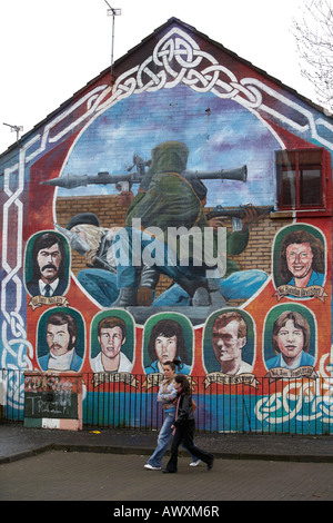 Due giovani donne a piedi passato un IRA di paramilitari memorial murale dotata di RPG e IRA sniper nei mercati zona di Belfast Foto Stock
