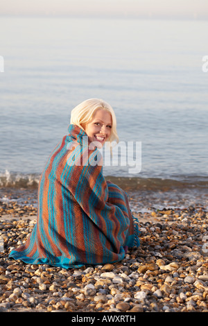 Giovane donna sorridente, seduto sulla spiaggia coperta in coperta, ritratto Foto Stock