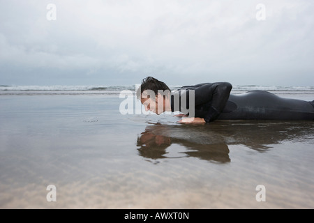 Uomo in wetsuit facendo pushups in acque poco profonde sulla spiaggia, vista laterale Foto Stock