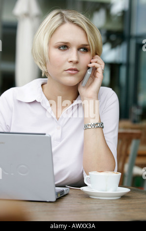 Giovane donna di affari con il cellulare e il computer portatile in un coffee shop Foto Stock