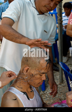 Parenti asciugare i capelli randagi a seguito della rasatura della testa di un giovane uomo tailandese, parte dell'ordinazione di un monaco novizio Foto Stock