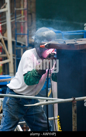 Un saldatore che indossa una maschera di sicurezza per proteggere il suo volto è visto sul posto di lavoro a un sito in costruzione. Foto Stock