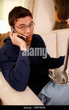 Giovane uomo che legge il giornale e parlando al cellulare Foto Stock