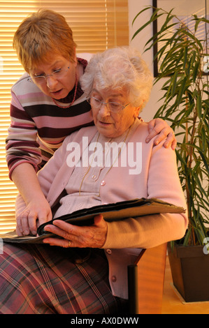 Donna anziana e sua figlia guardando attraverso un vecchio album di fotografie riempito con i ritratti di famiglia Foto Stock