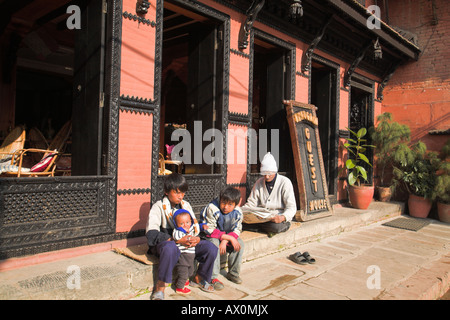 Il Nepal, Bhaktaphur, uomo si siede fuori Bhadgaon hotel reading con bambini seduti sulla fase Foto Stock