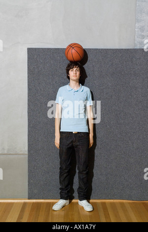 Un giovane uomo in piedi con una palla da basket bilanciato sulla sua testa Foto Stock