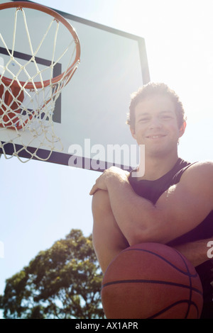 Un giovane uomo in piedi vicino a una piscina esterna Basketball hoop Foto Stock