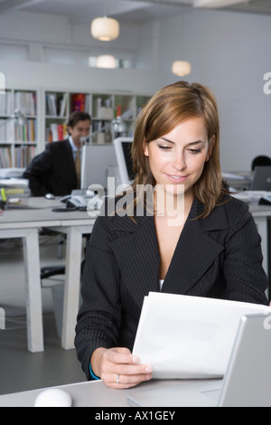 Una donna sta guardando un documento mentre seduti ad una scrivania in un ufficio Foto Stock