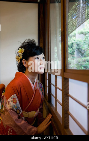 Una donna che indossa un kimono di guardare attraverso una finestra Foto Stock