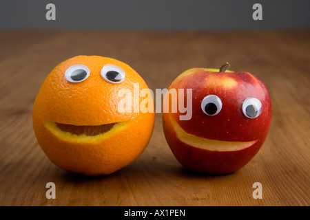 Un Apple e un arancio con bulbi oculari in plastica Foto Stock