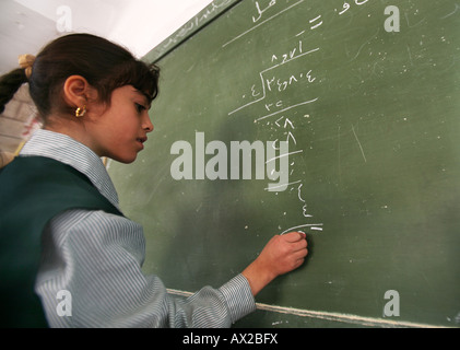 Una ragazza funziona su un problema di matematica alla lavagna nera a scuola molti rifugiati iracheni si sono insediati in Amman Giordania e i loro figli Foto Stock