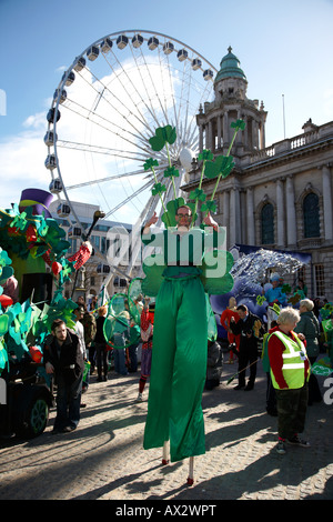 Stiltwalker vestito di verde che indossa trifogli a Belfast City Hall e la grande ruota prima della sfilata di carnevale e il giorno di San Patrizio Foto Stock