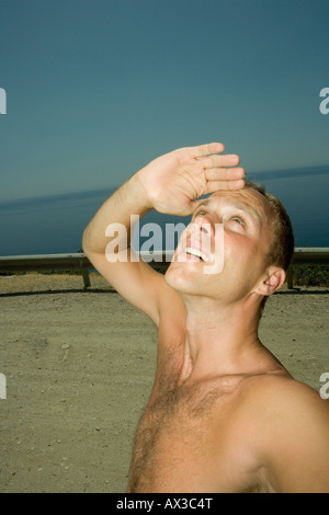Giovane uomo che copre la sua gli occhi e guarda il sole Foto Stock