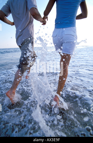 Coppia sulla spiaggia in esecuzione su acqua onda di bordo Foto Stock