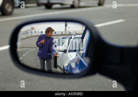 Immagine di una donna conducente, bloccati in una coda di auto, appena ottenere nella sua auto, come si è visto nell'ala specchio delle auto nella parte anteriore Foto Stock