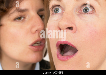 Due donne un sussurro segreto in close up di orecchio e bocca Foto Stock