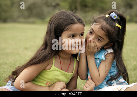 Ragazza whispering nella sua amica l orecchio in un parco Foto Stock