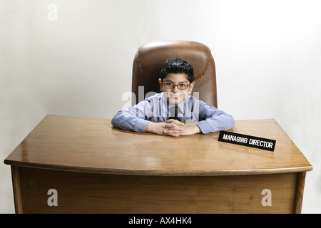 Ritratto di un ragazzo seduto in un ufficio e fingere come un uomo di affari Foto Stock