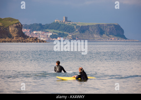 I surfisti si levano in piedi in profondità nel mare accanto alle tavole galleggianti a Cayton Bay, con il castello di Scarborough in lontananza. REGNO UNITO Foto Stock