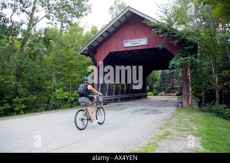 Una giovane donna corse la sua bici attraverso un ponte coperto nella città di Stowe vermont Foto Stock