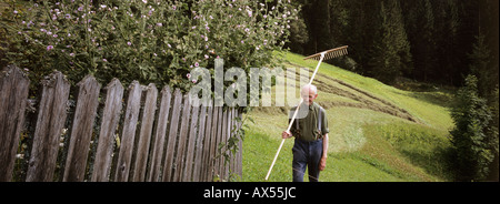 Senior man standing in giardino con rastrello sulla spalla Foto Stock