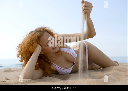Giovane donna sdraiata sulla spiaggia, giocando con sabbia Foto Stock
