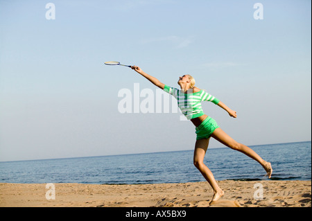Giovane donna giocando badminton sulla spiaggia Foto Stock