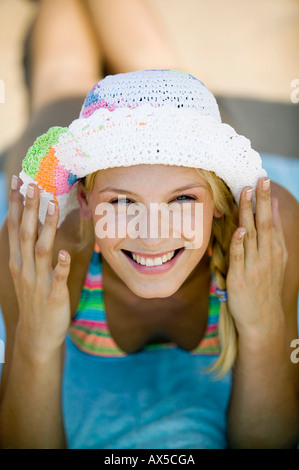 Giovane donna che indossa cappello giacente sulla spiaggia, sorridente, ritratto Foto Stock