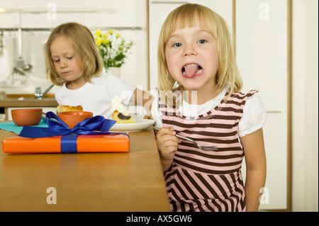 Due bambine (4-5) di mangiare la torta in cucina Foto Stock