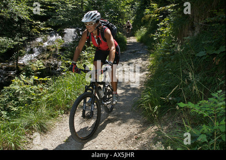 Biker femminile in mountain bike lungo un sentiero accanto ad un torrente a Samerberg, Baviera, Germania, Europa Foto Stock