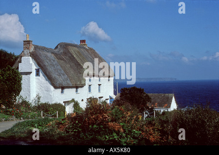 Cornovaglia, Inghilterra. Con il tetto di paglia tipici, imbiancato Cornish cottage con il mare oltre. Foto Stock