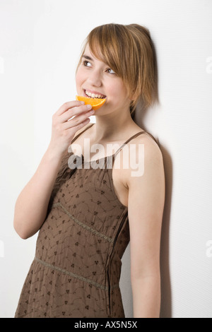 Giovane donna appoggiata contro una parete di mangiare una fetta di arancia Foto Stock