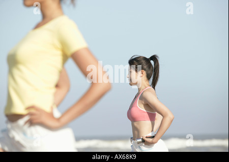 Due giovani donne stand in riva al mare con il manubrio in su della mano womans Foto Stock
