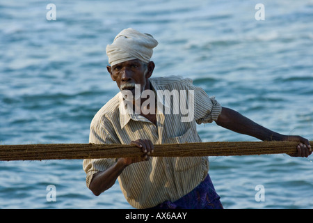 Uomo anziano tirando in reti da pesca sulla spiaggia di Varkala India Foto Stock