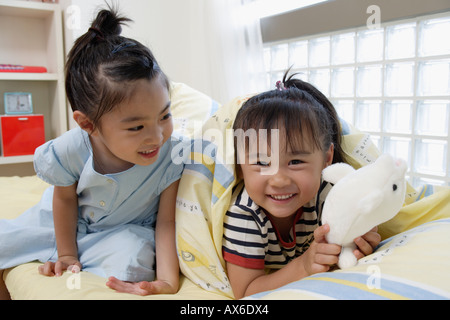 Sorelle in letto con un soffice bambola Foto Stock