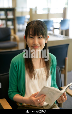 Una giovane donna si siede con un libro in mano come sorride alla telecamera Foto Stock